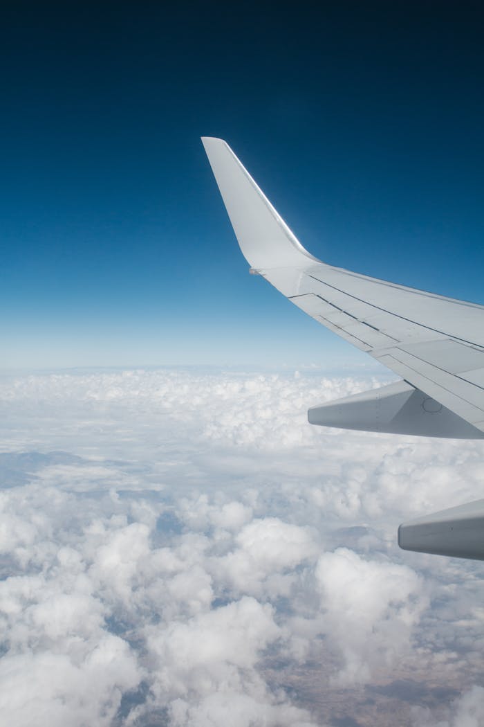 High-altitude view of airplane wing with white clouds and blue sky backdrop, perfect for travel themes.